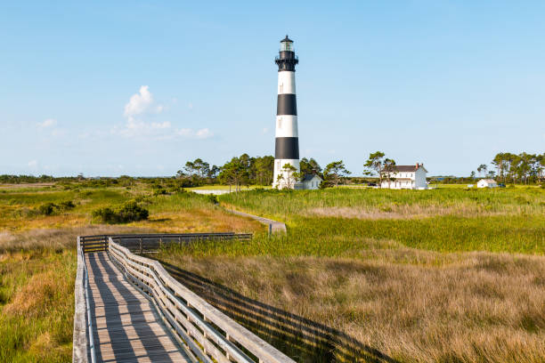 Wooden Ramp Over Marshland Leading to Bodie Island Lighthouse Wooden ramp over marshland, with a boardwalk trail to the Bodie Island lighthouse and surrounding buildings, on the Outer Banks of North Carolina near Nags Head. bodie island stock pictures, royalty-free photos & images