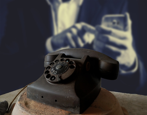 Black classic phone on a man hand typing on smartphone,Black antique vintage analog telephone dialing or scrolling phone on wooden table,Contact us concept.