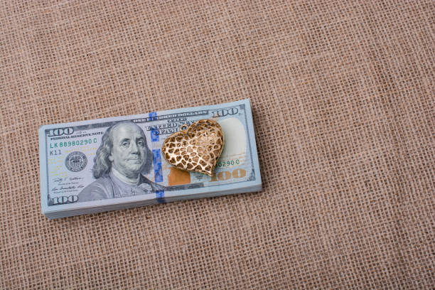 Bundle of US dollar and a heart shape heart icon bundle of US dollar placed on a linen canvas linen flax textile burlap stock pictures, royalty-free photos & images