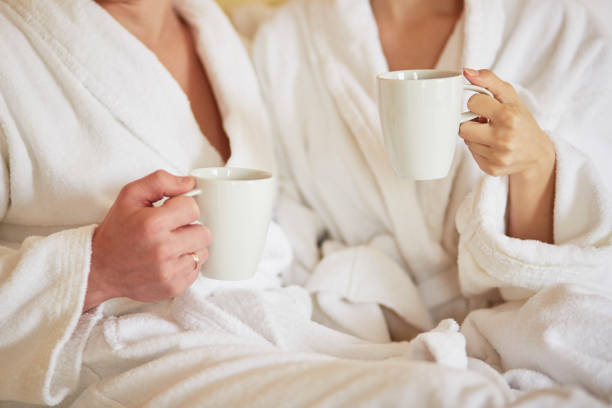 istock Couple in white bathrobes in bed, drinking coffee 821037954