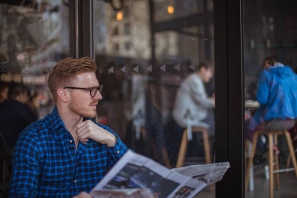 istock Young man reading newspaper in cafe 821052146