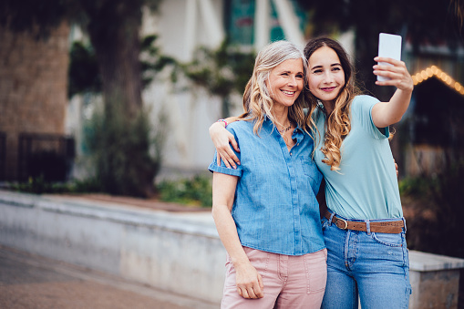 Beautiful modern grandmother and hipster granddaughter video calling on a smartphone in town