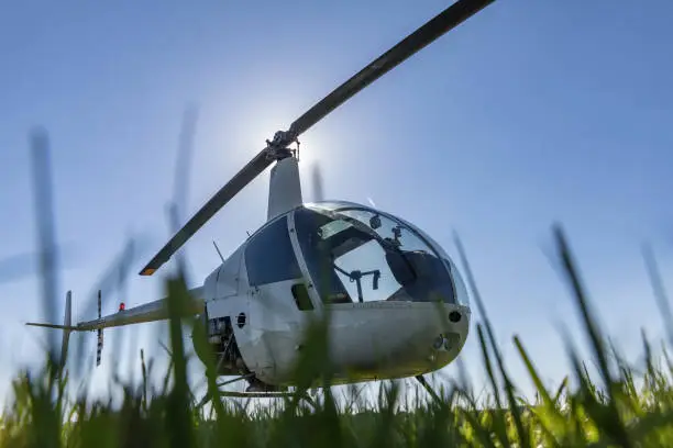 Small Robinson R22 light utility helicopter parked on grass airport. One of the world's most popular light helicopters with twin blades and a single engine