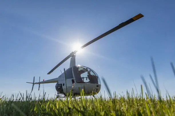 Photo of Small Robinson R22 light utility helicopter parked on grass airport. One of the world's most popular light helicopters with twin blades and a single engine