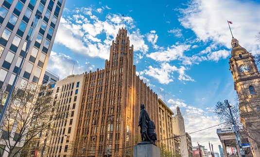 Melbourne, Australia September 17 2016: The art deco Manchester Unity Building in the Melbourne central business district against a blue sky with light clouds and Melbourne Town Hall clock tower.