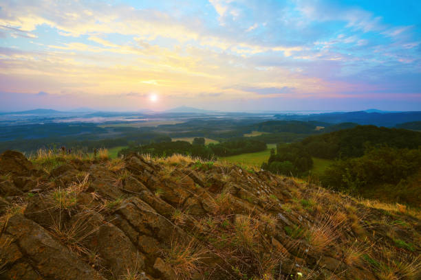 istock Sharp cliffs. Rocky basalt peak on hill. Forest valley  and Sun above horizon. 821154288