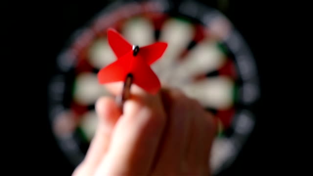 Slow motion of darts player throwing darts, defocused dart board on the background