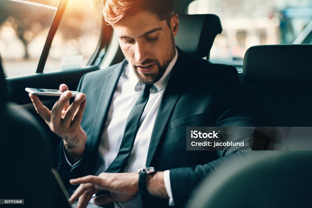 Businessman travelling by car using smart phone and checking time Handsome businessman talking on phone while sitting on the backseat of the car. Young man travelling by car using smart phone and checking time. Watch - Timepiece Stock Photo