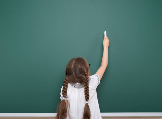 Schoolgirl writing chalk on a blackboard, empty space, education concept Schoolgirl writing chalk on a blackboard, empty space, education concept elementary student pointing stock pictures, royalty-free photos & images