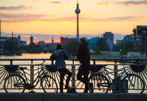 Berlin, Germany - June 10, 2012: Couple with bikes on bridge in silhouette. Enjoying the colorful Berlin sunset.  TV-tower in background.