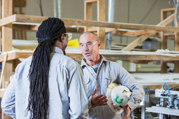 zwei männer arbeiten in einer kleinen fabrik, die diskussion - minority african ethnicity business hardhat stock-fotos und bilder