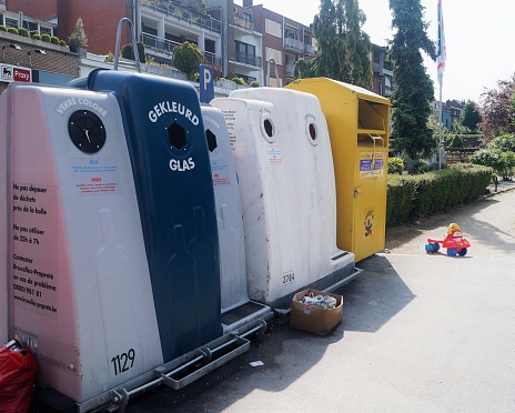 Uccle, Belgium – May 28, 2017. Public receptacles for collecting colored and clear glass bottles in a residential area outside an apartment building. Recycling concept