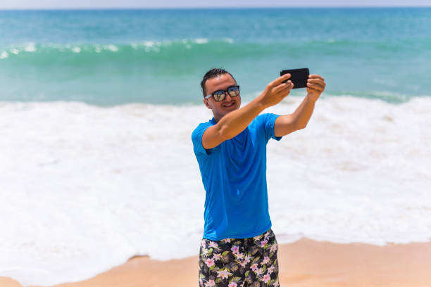 istock Happy handsome smiling man on vacation laughing at the beach taking selfie 821210168