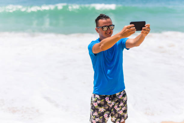 istock Happy handsome smiling man on vacation laughing at the beach taking selfie 821210216