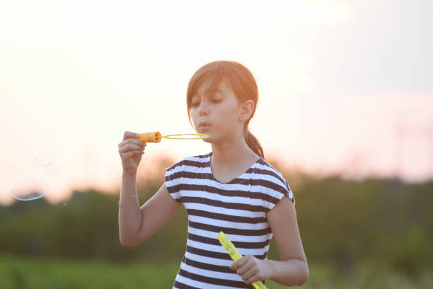 istock Little girl blowing soap bubbles in a field at sunset 821227962