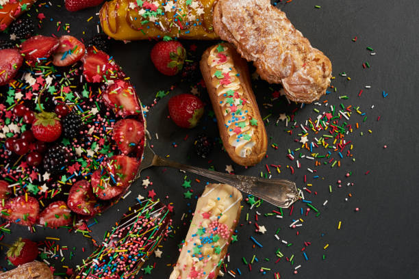Fresh delicious colourful eclairs and summer berry cake with berries strawberries blackberries currants on dark stone background with copy space. Top view
