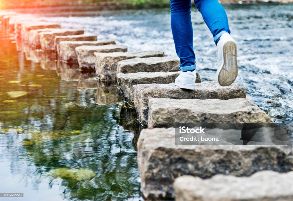 Femme traversant les pierres de progression sur une rivière - Photo de Pas à pas libre de droits