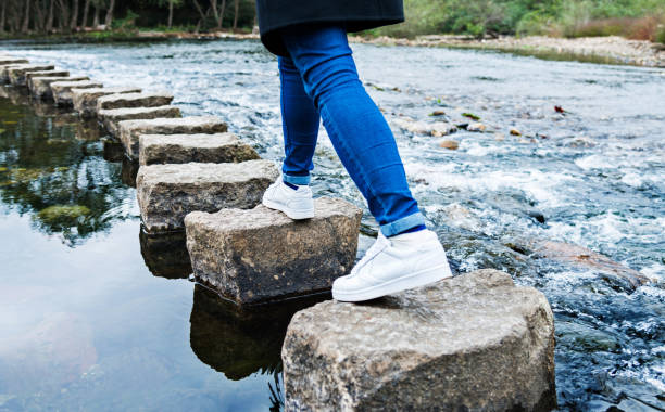 femme traversant les pierres de progression sur une rivière - stepping stone stone stepping footpath photos et images de collection