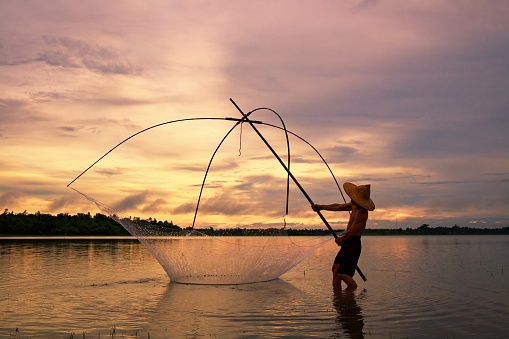 Fisherman on silhouette sunrise with gear fishing on the lake is a culture of Thai or Laos people's