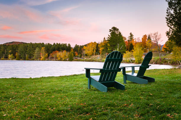 Green Adirondack Chairs on the Shore of a Lake Empty Adirondack Chairs Facing a Lake at Dusk. Beautiful Autumn Colours in Background. mirror lake stock pictures, royalty-free photos & images