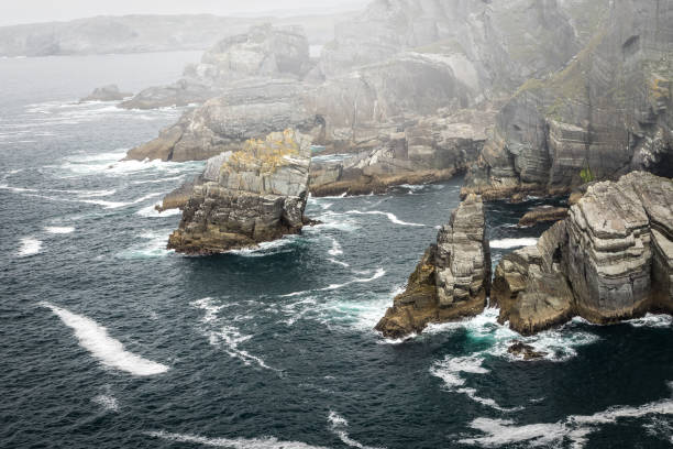 Rocky headland, waves breaking on the coastline, and mist Rocky headland at Mizen Head, County Cork, Ireland, with waves from the Atlantic ocean breaking on the coastline, and mist. mizen head stock pictures, royalty-free photos & images