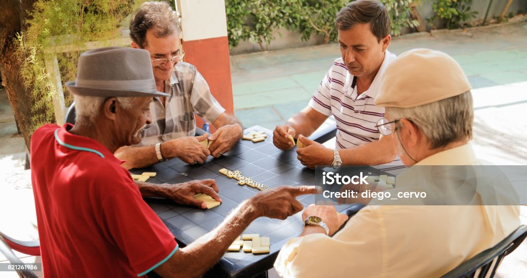 Active Retirement Happy Old Friends Playing Domino Game Retired people, seniors and free time. Old latino men having fun and playing game of domino in Cuba. Domino Stock Photo