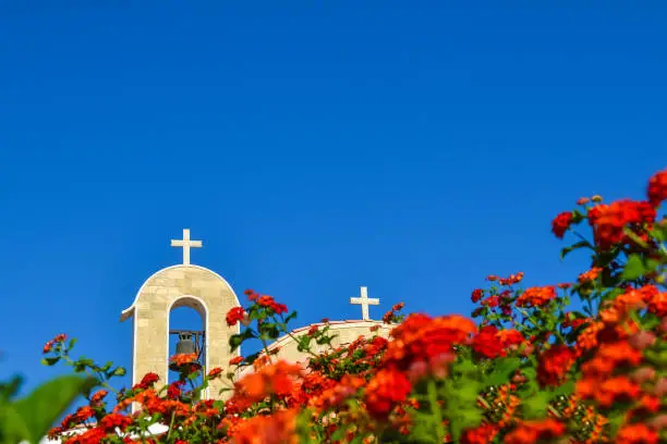 Orthodox church with a tiled roof and a bell. Red roses in the foreground. Cyprus. Ayianapa. Church of St. Epiphany.