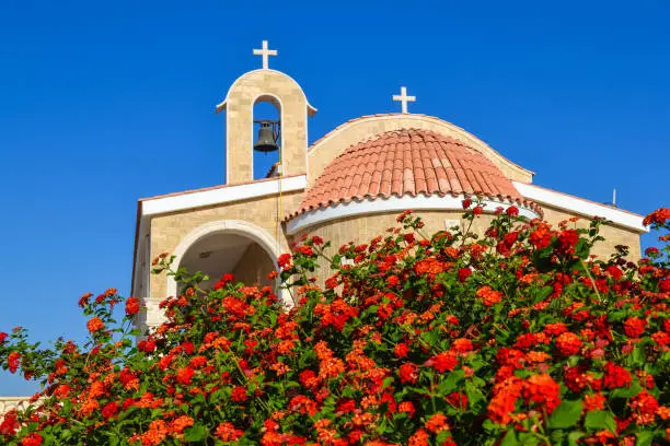 Orthodox church with a tiled roof and a bell. Red roses in the foreground. Cyprus. Ayianapa. Church of St. Epiphany.