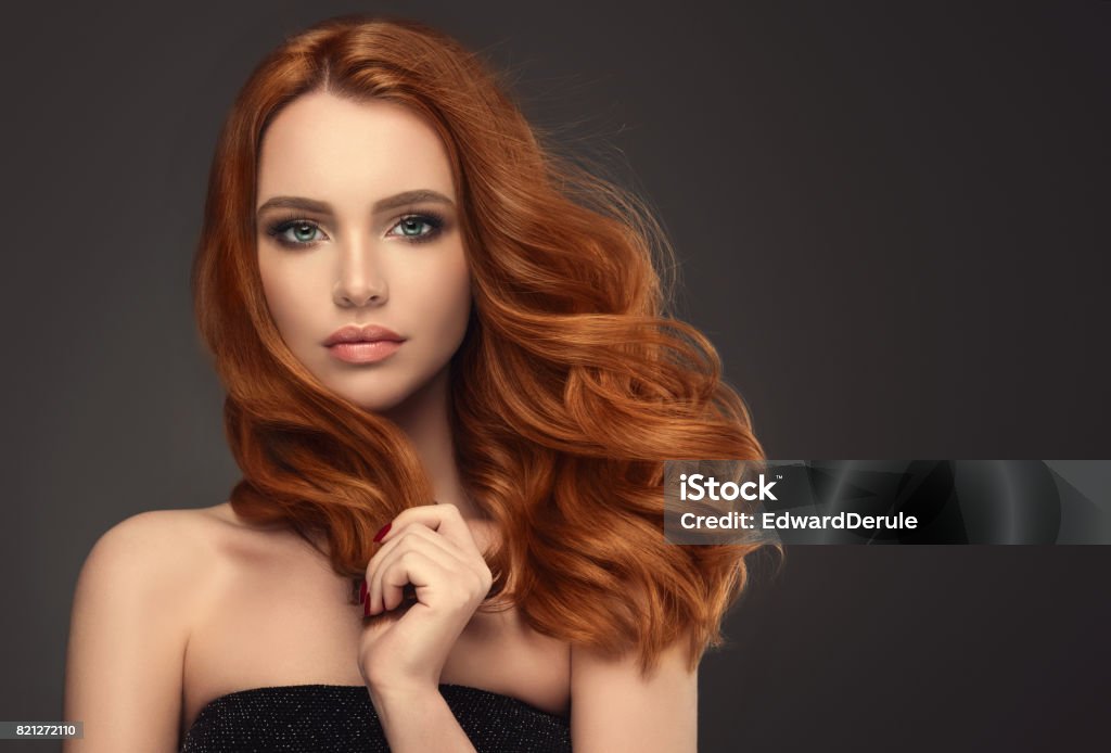 Red haired woman with voluminous, shiny and curly hairstyle.Flying hair. Young red haired woman  with voluminous, shiny and wavy hair . Beautiful model with long, dense and curly hairstyle. Flying hair. Hair Stock Photo