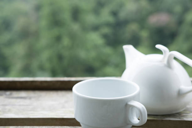 white tea cup and mug on wooden table with green nature background