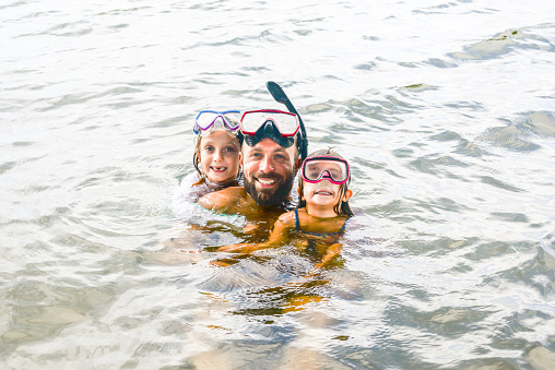 Two Children and a man in the water ocean in snorkel gear smiling for the camera
