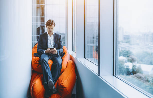 istock Businessman chilling with smartphone on orange pillows 821404208