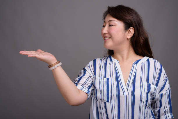 scatto in studio di matura bella donna d'affari asiatica su sfondo grigio - donna profilo braccia alzate foto e immagini stock