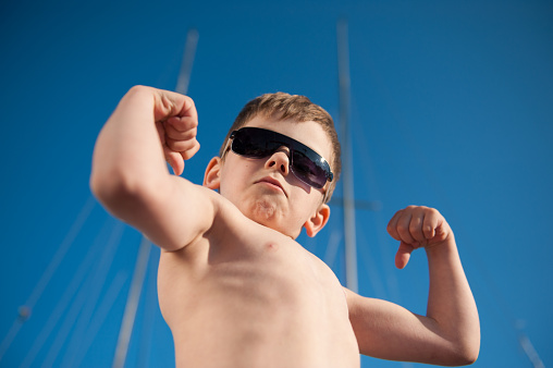 healthy preschool child in black sunglasses showing his biceps