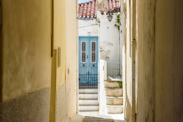 Narrow laneway in Chora old town Andros Island Greece with blue door at end.