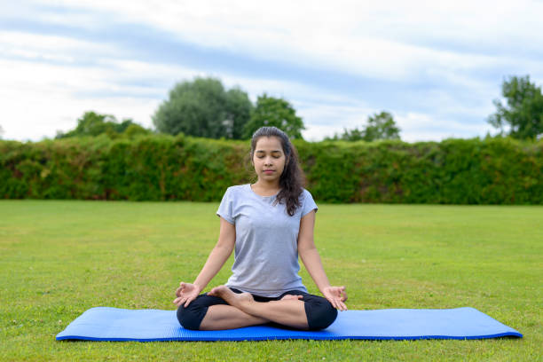 Teenage girl practising yoga outdoors Portrait of teenage girl practising yoga on mat outdoors, Lotus  Position sukhasana stock pictures, royalty-free photos & images
