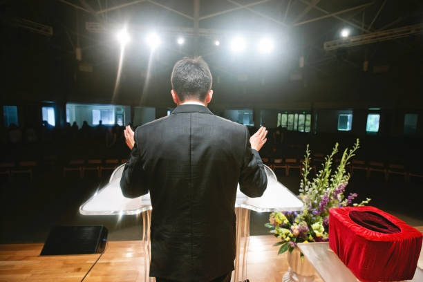 Pastor praying for congregation A pastor stands behind the pulpit in front of a congregation protestantism stock pictures, royalty-free photos & images