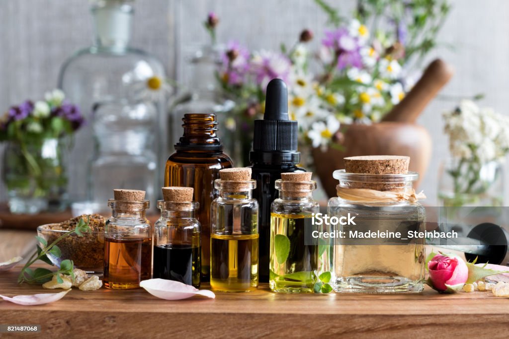 Selection of essential oils Selection of essential oils, with herbs and flowers in the background Herbal Medicine Stock Photo