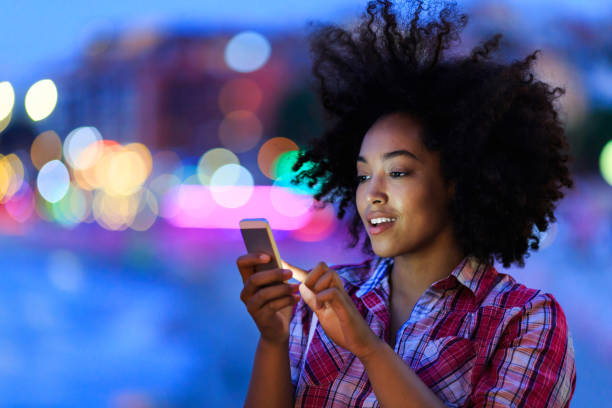 Young woman using smart phone at night on street Attractive woman having fun on street, using smart phone at night. mobile phone lights up stock pictures, royalty-free photos & images