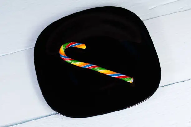 Candycane. Bright striped candy on a black plate and a pale cornflower blue wooden background