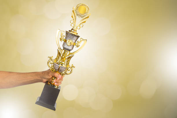 istock Man's hand holding golden winner trophy cup on blurred golden bokeh background 821521494