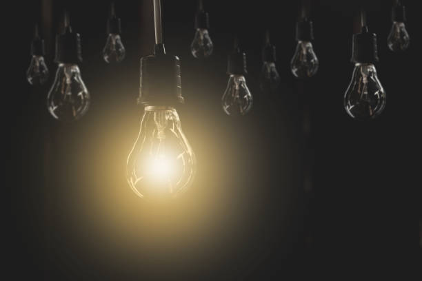 istock Hanging light bulbs with glowing one on dark background. Idea and creativity concept with light bulbs. 821540340