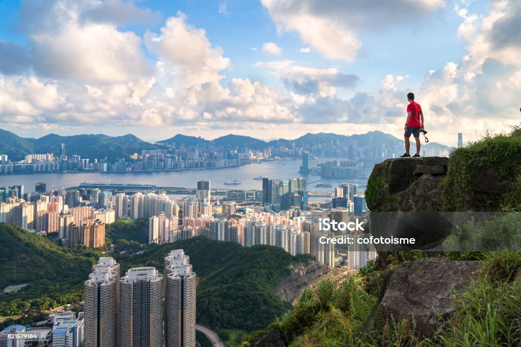 fotografo in piedi sulla cima di Cliff sopra il paesaggio urbano di Hong Kong - Foto stock royalty-free di Hong Kong