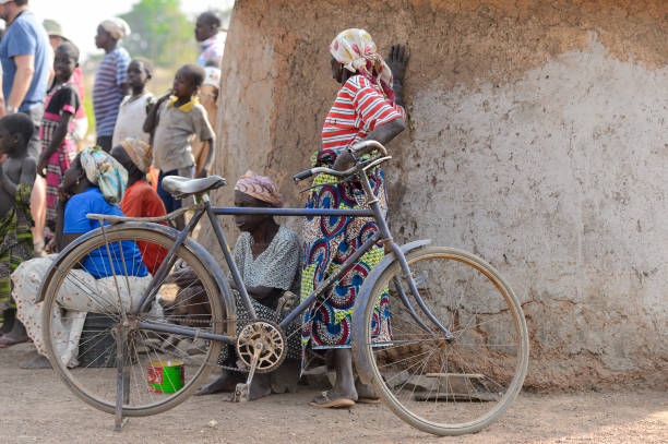 GHANI, GHANA - JAN 14, 2015: Unidentified Ghanaian woman in a headscarf with a bike stands near a mud house. Local people call her a witch.