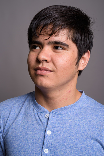 Studio shot of young Asian teenage boy wearing blue shirt against gray background vertical shot