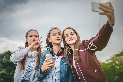 three happy teenage girls taking selfie outdoors