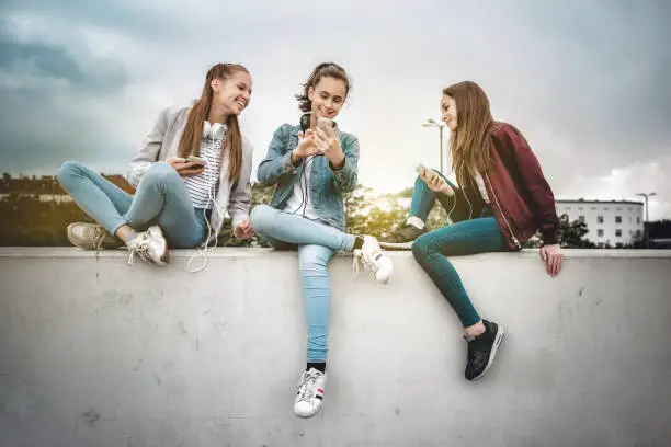 Photo of three teenage girls with smartphones on concrete wall