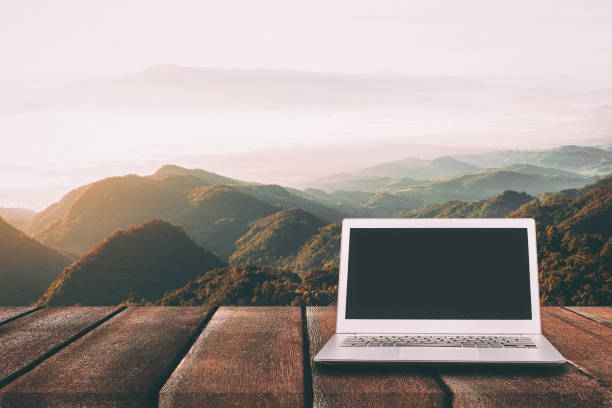 istock Laptop with blank screen on wooden table with forest in mountain and pine trees background, can used for display or montage your products 821619178