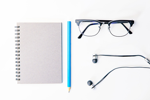 Top view of business working place with notepad,modern glasses,earphone on white table,flatlay concept.