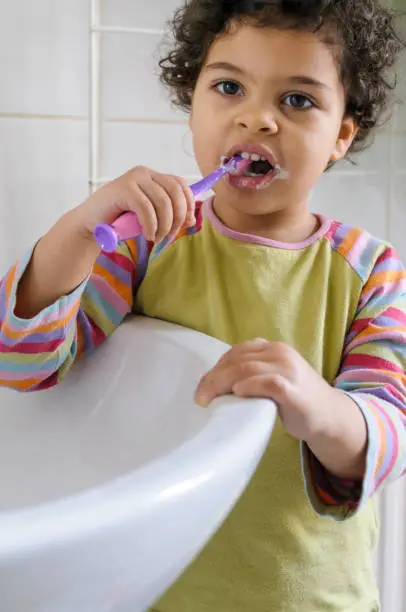 Stock photo of a little girl brushing her teeth on her own. This file has a signed model release.